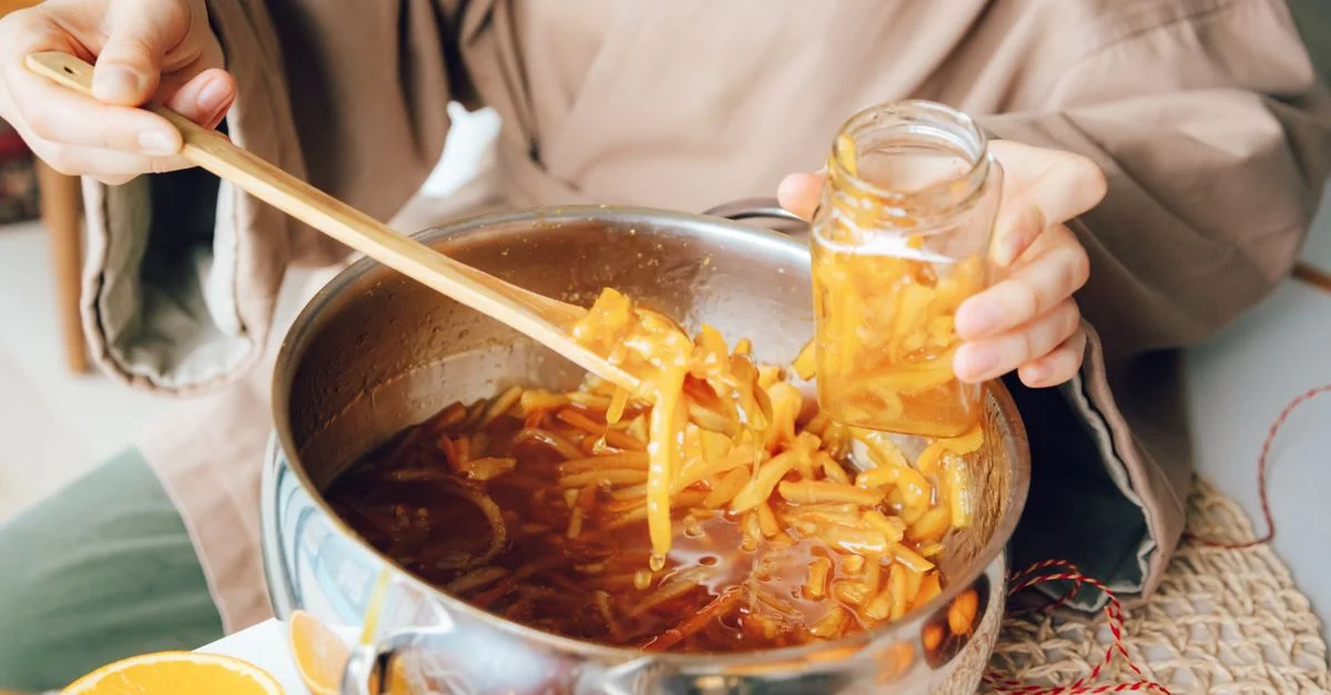 Mains préparant de la marmelade d'agrumes maison dans une scène de cuisine avec des oranges fraîches.
