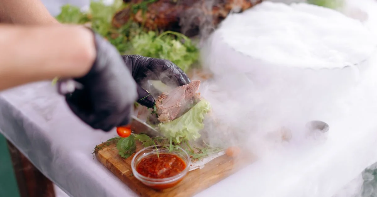 Chef préparant un plat gastronomique avec effet de fumée et ingrédients décoratifs sur une planche à découper.