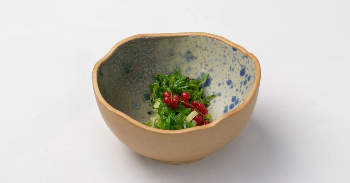 Gros plan d'une salade d'algues vertes fraîches avec des baies rouges dans un bol en céramique artisanal.