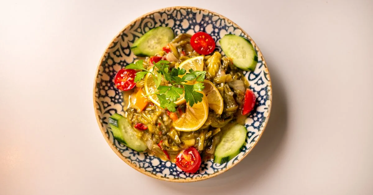 Vue de dessus d'une salade de légumes vibrante avec citron, concombre et persil dans un bol décoratif.