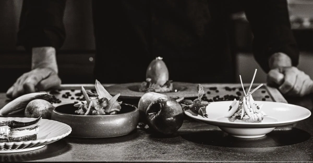 Un chef arrange des plats gastronomiques sur une table dans un cadre en noir et blanc.