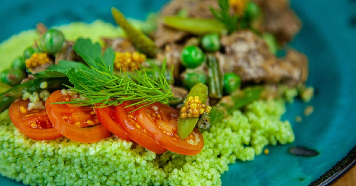 Gros plan d'une salade colorée de couscous vert avec des tomates et des herbes fraîches.