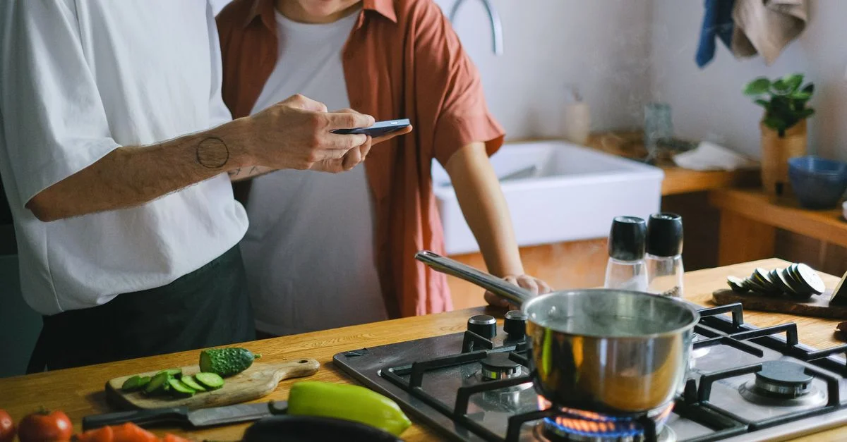 Un couple qui cuisine ensemble et utilise un smartphone pour des recettes dans une cuisine conviviale.