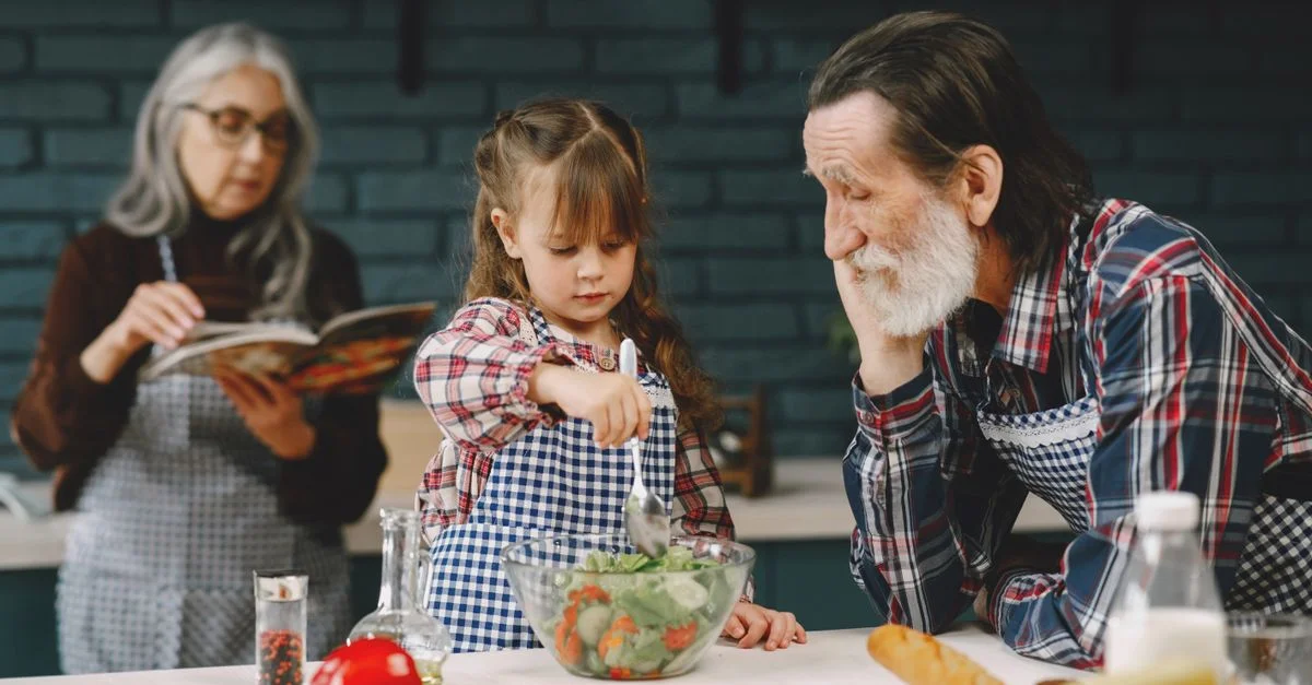 Grand-père et petite-fille préparent une salade pendant que grand-mère lit une recette.